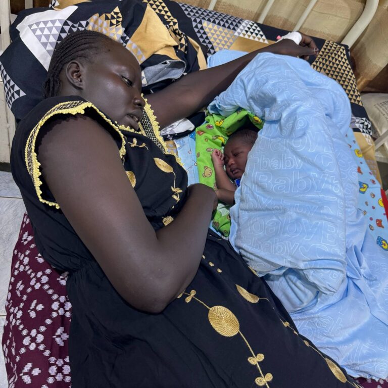 A woman lovingly holds a sleeping child wrapped in a blue blanket.